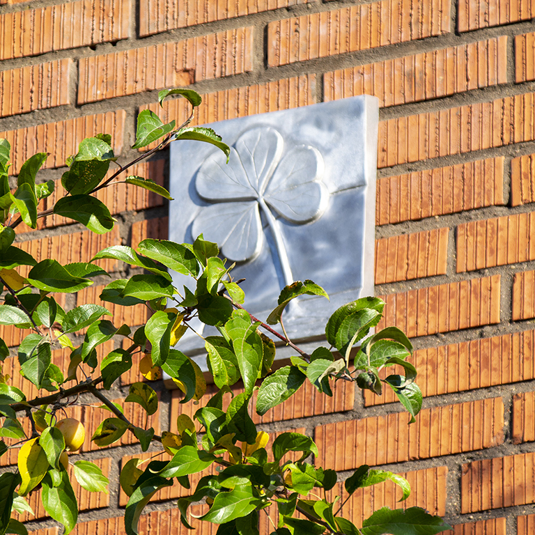 Treklöverns klöver som metallskylt på en tegelfasad.